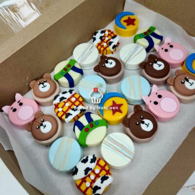 Assorted colorful fondant-covered cookies in a box, featuring bear and pig faces, gift-box patterns, rockets, stars, and pastel circles.
