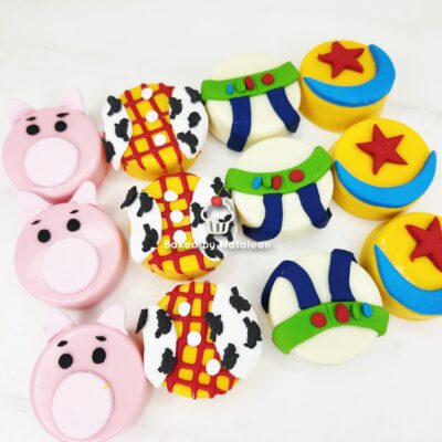 Assorted decorated cookies: pink pig faces, cow-print lattice circles, green-and-blue space helmets, and yellow-with-star designs.
