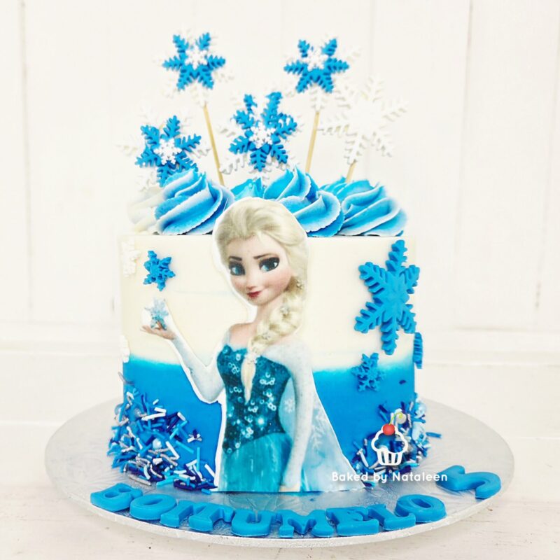 Frozen-themed birthday cake with an Elsa figure, blue frosting swirls, and blue snowflakes.