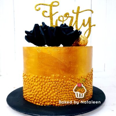 Gold cake with a black ruffle flower and glittery gold 'Forty' topper on a black base, festive celebration dessert