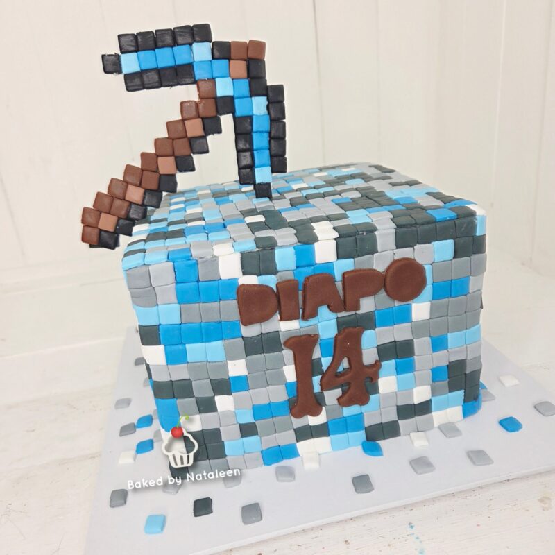 Minecraft-style square mosaic cake in blue, gray, and white tiles with a pixelated brown and blue pickaxe on top; brown tiles form the name 'DINO' and the number '14'.
