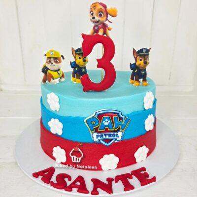 Paw Patrol birthday cake with blue and red tiers, white paw prints, a large red '3' topper, and Paw Patrol figures on top.