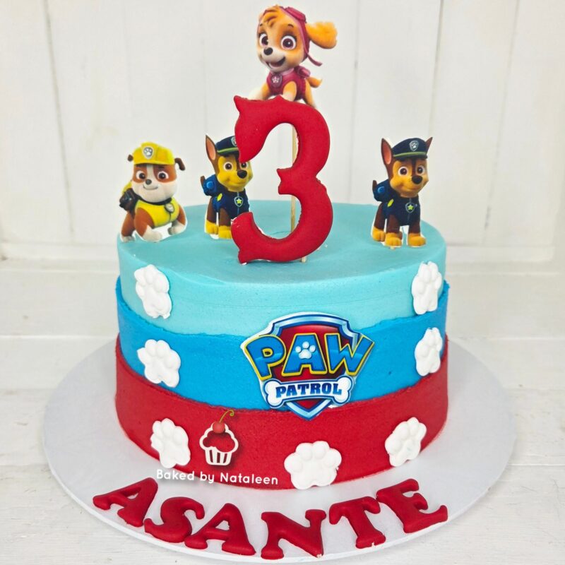 Paw Patrol birthday cake with blue and red tiers, white paw prints, a large red '3' topper, and Paw Patrol figures on top.