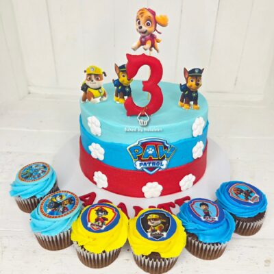 Cake decorated with Paw Patrol characters and a large red 3 candle, blue and red fondant with white paw prints and cupcakes around it.